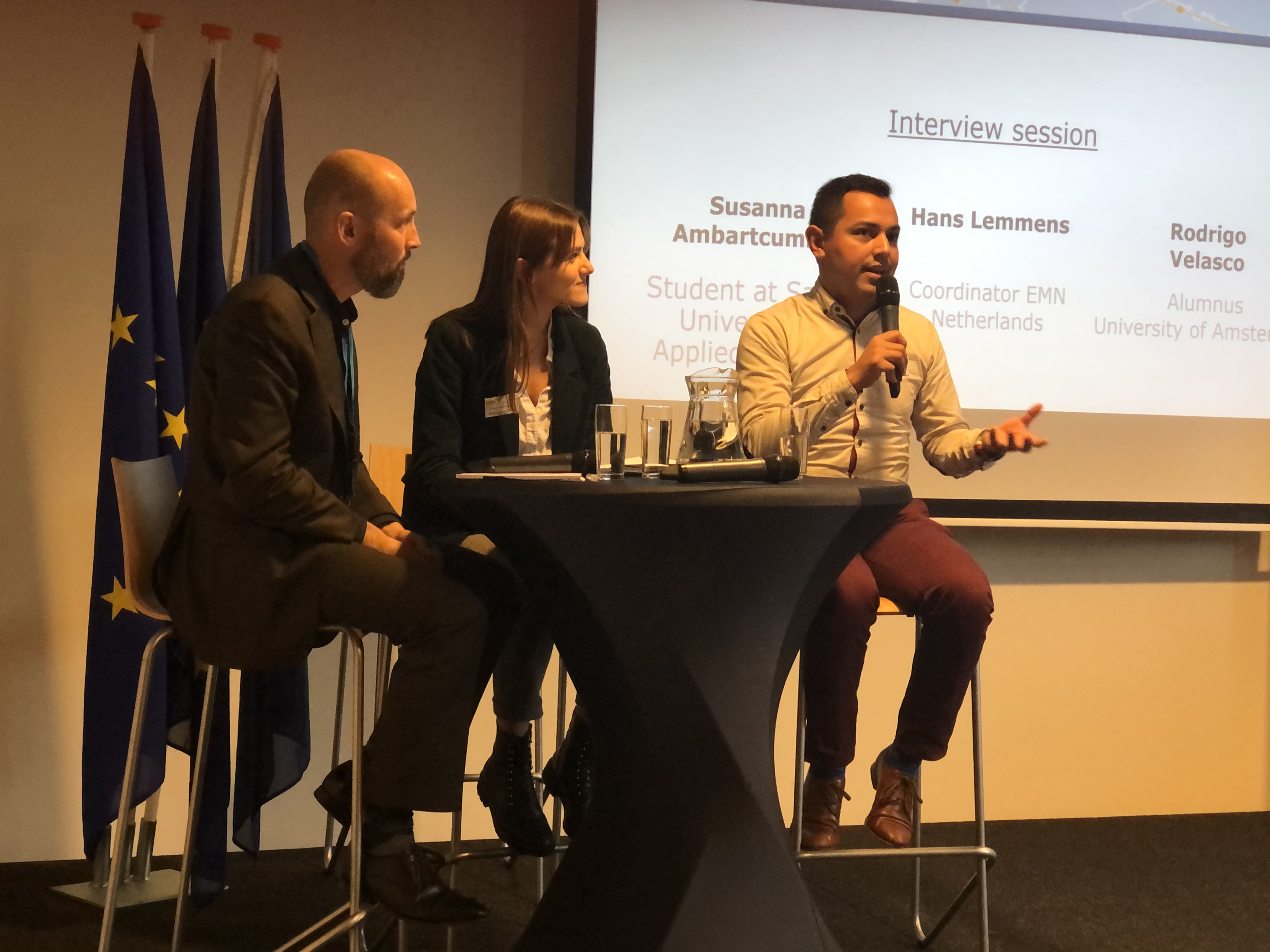 Internationale studenten Rodrigo Velasco (Mexicaans) en Susanna Ambartcumian (Russisch/Armeens) in gesprek met Hans Lemmens, coördinator EMN Nederland