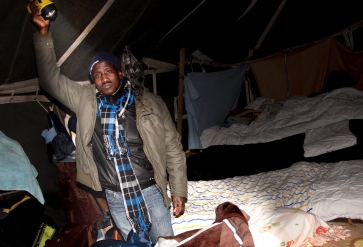 In het schijnsel van zijn zaklamp toont een migrant, die illegaal in Nederland is, zijn slaapplaats in een tentenkamp in Osdorp. | Foto: Erixphotobook | Nationale Beeldbank
